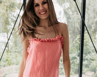May include: A coral pink linen dress with a ruffled neckline. The dress is sleeveless and has a relaxed fit.