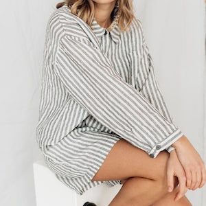 May include: A woman wearing a white and gray striped linen shirt and shorts set. The shirt has a button-down collar and long sleeves. The shorts are a relaxed fit and have a wide leg.