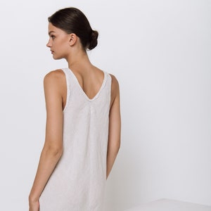Puede incluir: Un vestido blanco de lino con finas rayas verticales. El vestido tiene un escote redondo y es sin mangas.