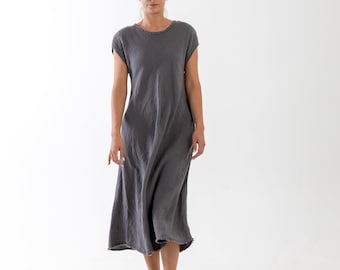 May include: A charcoal gray midi-length dress with short sleeves, a round neckline, and a raw, frayed hemline. The garment features a relaxed, loose-fitting silhouette and is paired with metallic gold strappy sandals with flat soles.