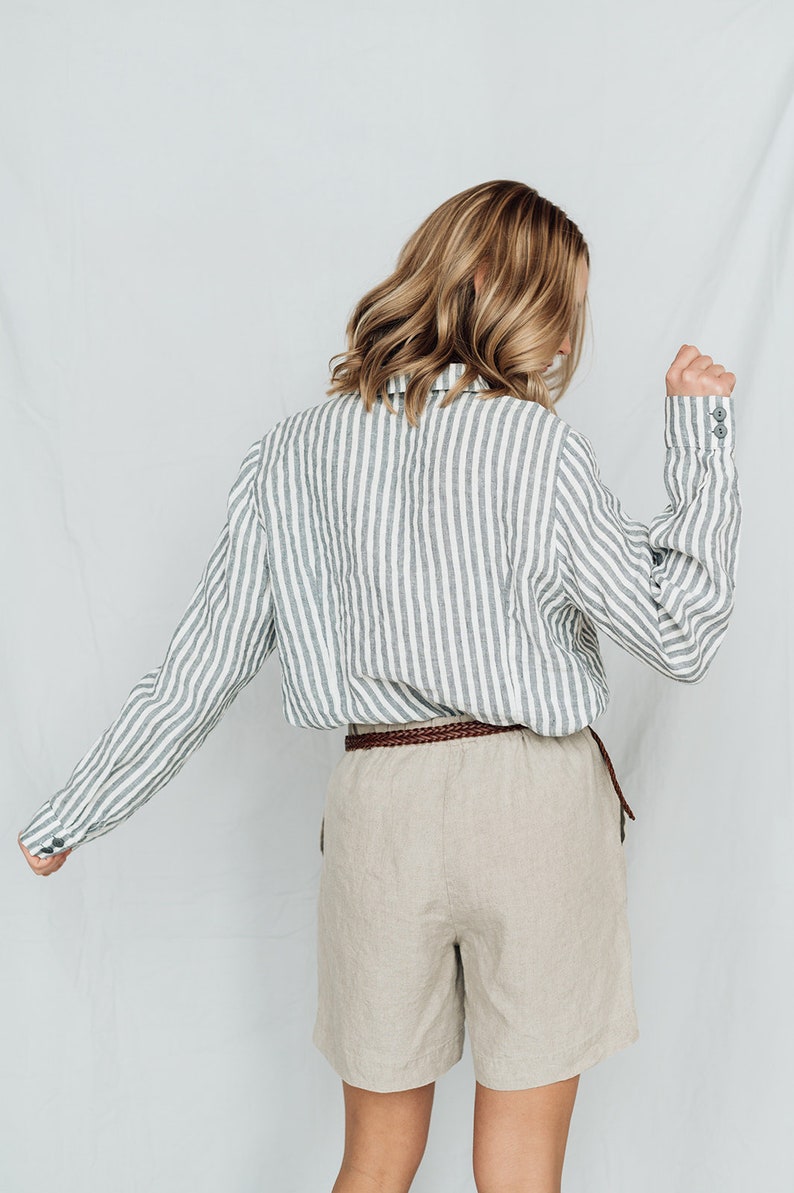 May include: A woman wearing a striped linen shirt with a brown braided belt and beige linen shorts.