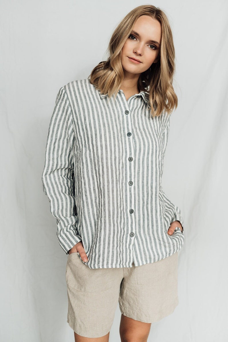 May include: A woman wearing a white and gray striped linen shirt with a button-down collar and long sleeves. She is also wearing beige linen shorts.