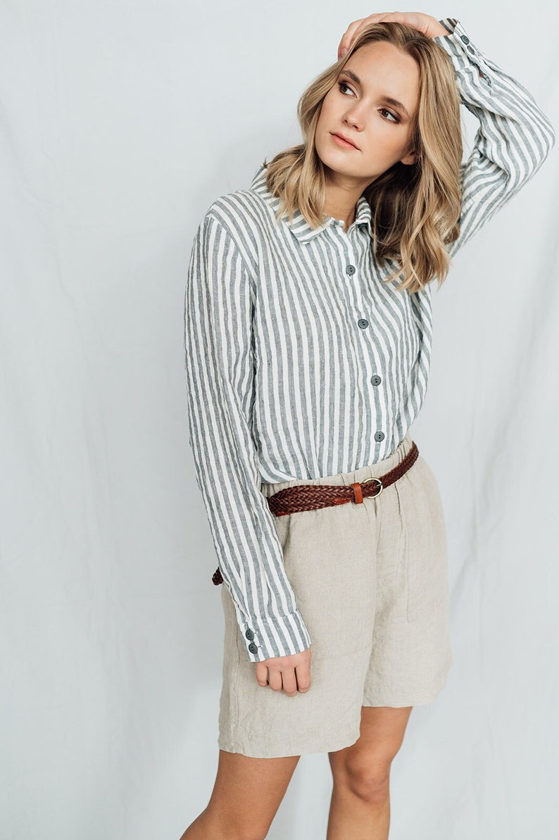 May include: A woman wearing a striped linen shirt with a brown braided belt and beige linen shorts.