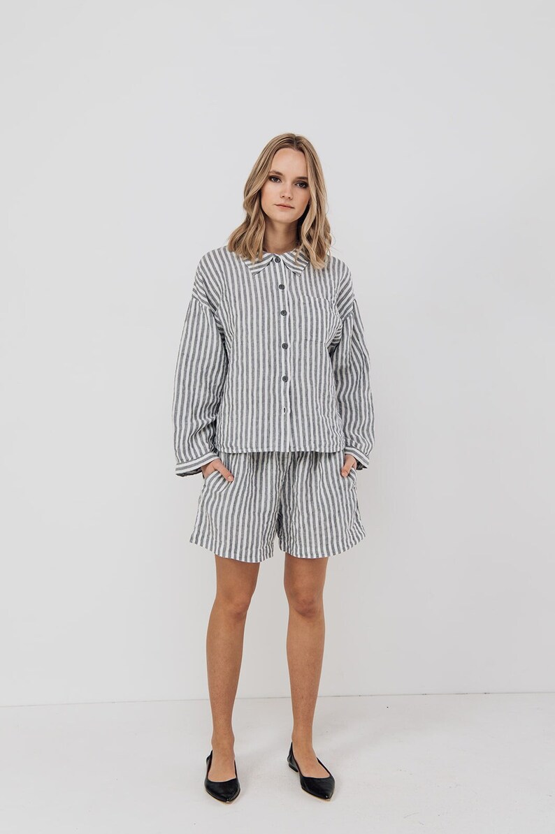 May include: A woman is wearing a white and gray striped shirt and matching shorts. The shirt has a button-up front and long sleeves. The shorts are a relaxed fit and have a drawstring waist.