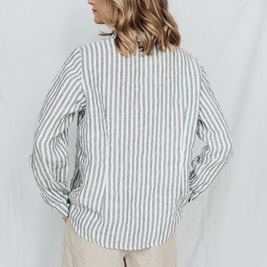May include: A white and gray striped linen shirt with long sleeves and a button-up collar. The shirt is tucked into a pair of beige linen shorts.