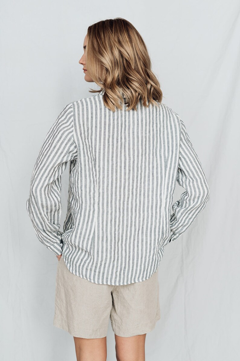 May include: A white and gray striped linen shirt with long sleeves and a button-up collar. The shirt is tucked into a pair of beige linen shorts.