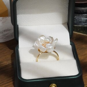 May include: A white pearl flower ring with a gold band. The ring is in a green velvet ring box.