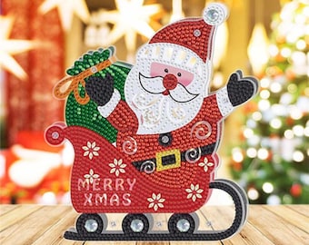 May include: A red and white Santa Claus figure holding a green bag with a gold bow, riding in a red sleigh with the words "Merry Xmas" on the side. The sleigh has four black wheels.