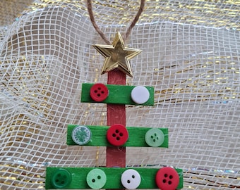 Può includere: Un ornamento per albero di Natale verde e rosso realizzato con bastoncini di ghiacciolo e bottoni. L'albero è decorato con una stella dorata in cima e ha un nastro a scacchi rosso e bianco in fondo.
