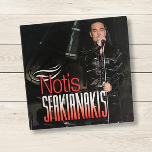 Könnte beinhalten: Eine CD-Hülle mit Notis Sfakianakis. Das Albumcover hat einen schwarzen Hintergrund mit einem Foto des Sängers in schwarzer Kleidung, der ein Mikrofon hält. Der Name des Künstlers ist rot.