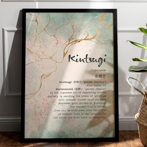 Op de afbeelding: Een ingelijst afdruk met een aquarel achtergrond en gouden accenten. De afdruk toont het woord "Kintsugi" in zwarte tekst met het Japanse woord ervoor in gouden tekst eronder. De definitie van Kintsugi is in zwarte tekst onder het Japanse woord geschreven.