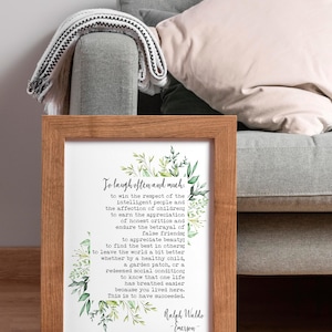 May include: A framed print with a white background and green floral accents. The print features a quote by Ralph Waldo Emerson: "To laugh often and much... This is to have succeeded."
