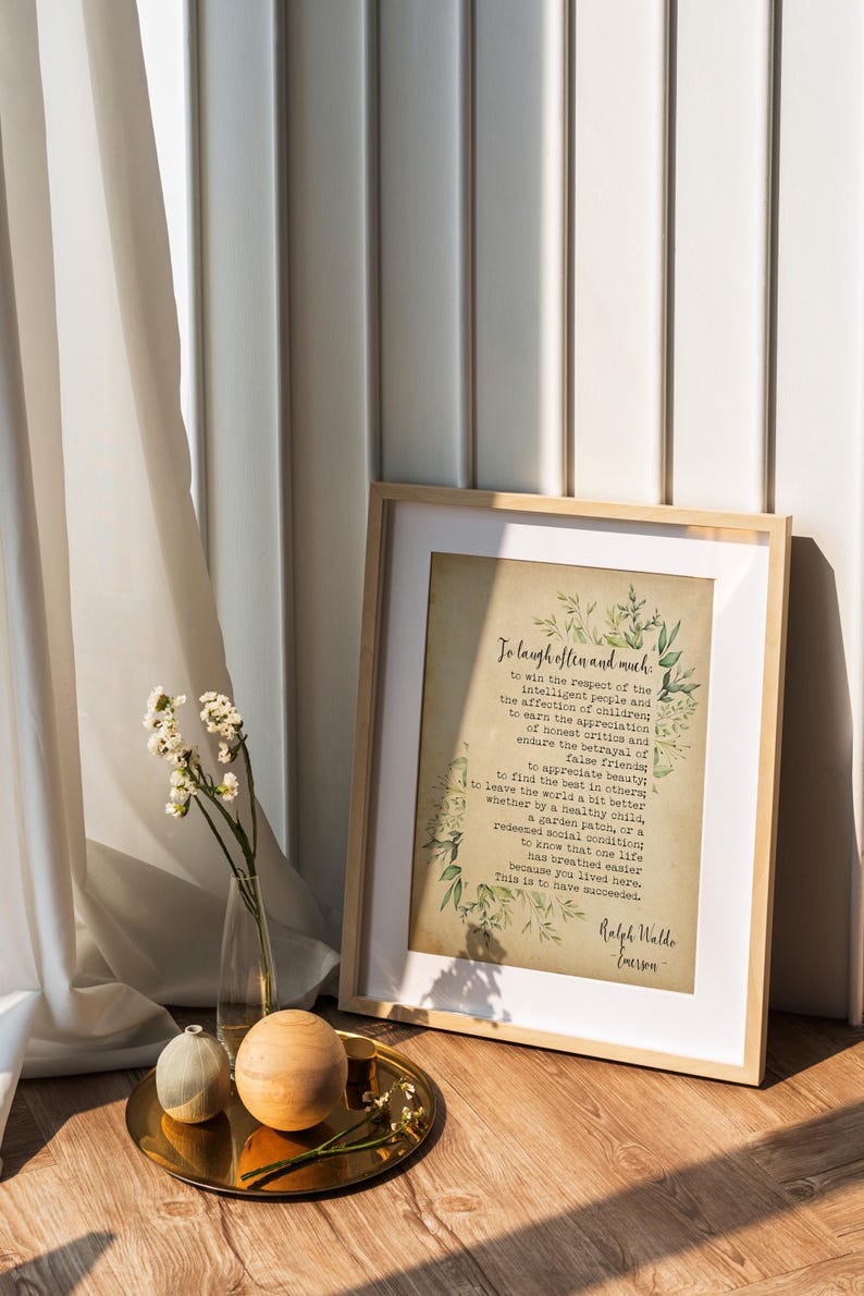 May include: A framed print with a quote by Ralph Waldo Emerson on a vintage-style background with green foliage. The quote reads "To laugh often and much... This is to have succeeded."