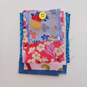 May include: A stack of fabric scraps in various shades of blue, pink and white with a floral pattern. A yellow button is sewn onto the top scrap.