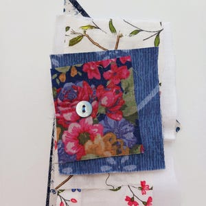 May include: A selection of fabric offcuts in diverse patterns and colours. A square of floral fabric with a button is the central piece. Other fabrics include a blue striped piece, and white fabrics with floral and bird designs.