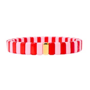 Könnte beinhalten: Ein rosa-rotes gestreiftes Armband mit einer goldenen Perle in der Mitte.