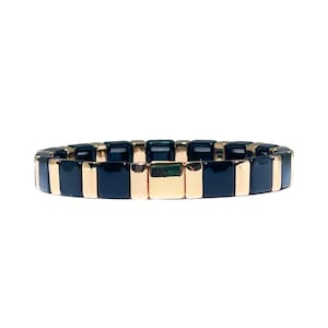 Könnte beinhalten: Ein Armband mit einem sich wiederholenden Muster aus marineblauen und goldenen rechteckigen Kacheln. Das Armband besteht aus kleinen, quadratischen Kacheln, die sich zwischen einem dunklen Marineblau und einer glänzenden Goldfarbe abwechseln. Das Armband ist für das Handgelenk konzipiert.