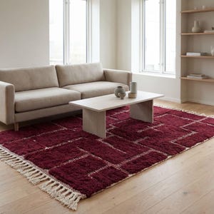Deep red wool rug handcrafted in Morocco with thick textured pile and rich natural fibers. This handmade area rug features a warm deep red tone, soft plush surface, and subtle Berber-inspired design. Ideal for living rooms or bedrooms, the rug adds warmth, depth, and authenticity while offering durable, eco-friendly wool construction and customizable sizing.
