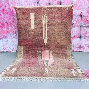May include: A pink and brown Moroccan rug with a geometric pattern. The rug has a fringe border and is made of wool.