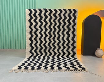 May include: A large, rectangular rug with a cream-colored background and a bold, black zigzag pattern. The rug has a thick, textured pile and a fringe along the bottom edge. The rug is suitable for a living room or bedroom.
