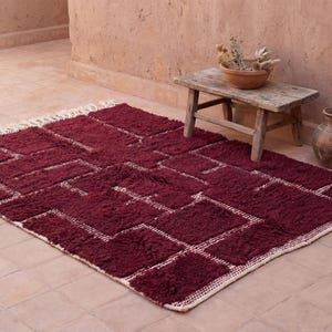 May include: A burgundy geometric rug with a white border and accents. The rug is rectangular and has a plush texture. The design features a series of interconnected rectangles and squares.