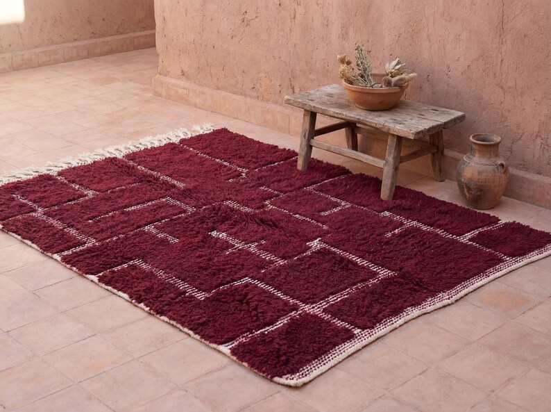 May include: A burgundy geometric rug with a white border and accents. The rug is rectangular and has a plush texture. The design features a series of interconnected rectangles and squares.