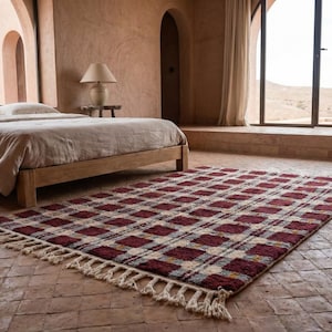 Puede incluir: Una alfombra rectangular con un dise&ntilde;o de cuadros en tonos burdeos, crema y gris. La alfombra tiene flecos en los extremos cortos y est&aacute; colocada sobre un suelo de baldosas en un dormitorio. La habitaci&oacute;n tiene una cama y una ventana.