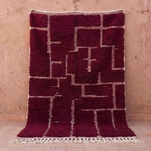 Handmade burgundy Moroccan rug woven from 100% natural wool, featuring a plush high-pile texture with minimalist Berber line motifs in soft ivory. This deep burgundy wool rug is handwoven by Moroccan artisans, offering warmth, durability, and a cozy modern look. Ideal as a living room or bedroom area rug, perfect for Scandinavian, boho, and warm minimalist interiors.