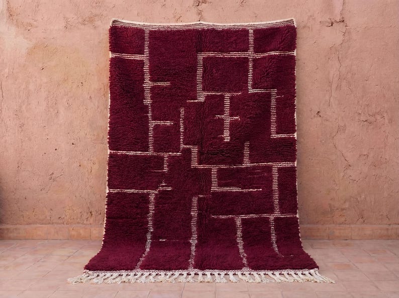Handmade burgundy Moroccan rug woven from 100% natural wool, featuring a plush high-pile texture with minimalist Berber line motifs in soft ivory. This deep burgundy wool rug is handwoven by Moroccan artisans, offering warmth, durability, and a cozy modern look. Ideal as a living room or bedroom area rug, perfect for Scandinavian, boho, and warm minimalist interiors.
