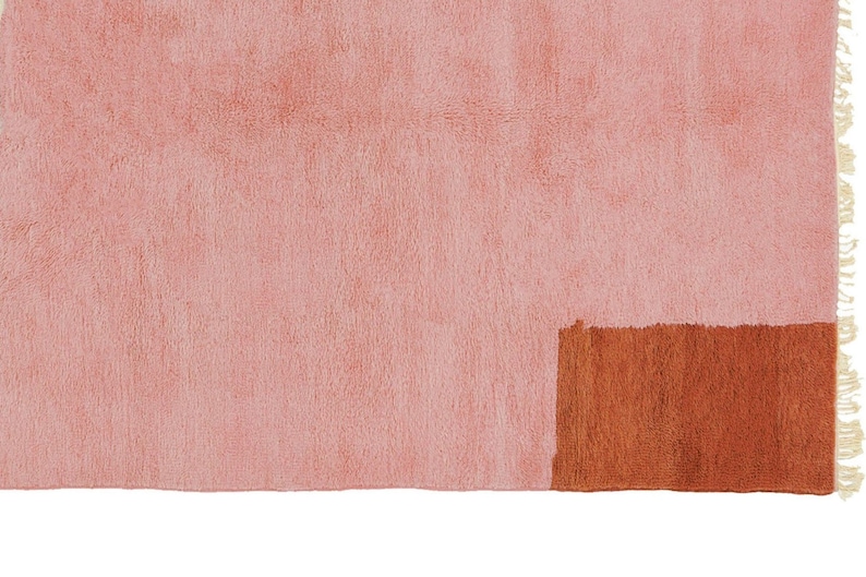 K&ouml;nnte beinhalten: Ein rosa-brauner Teppich mit Fransenrand. Der Teppich hat ein geometrisches Design mit einem einfarbigen rosa Abschnitt und einem braunen Rechteck.