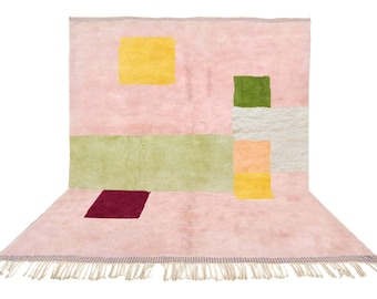 Könnte beinhalten: Ein rosa Teppich mit einem geometrischen Muster in Grün-, Gelb- und Rottönen. Der Teppich hat einen Fransenrand.
