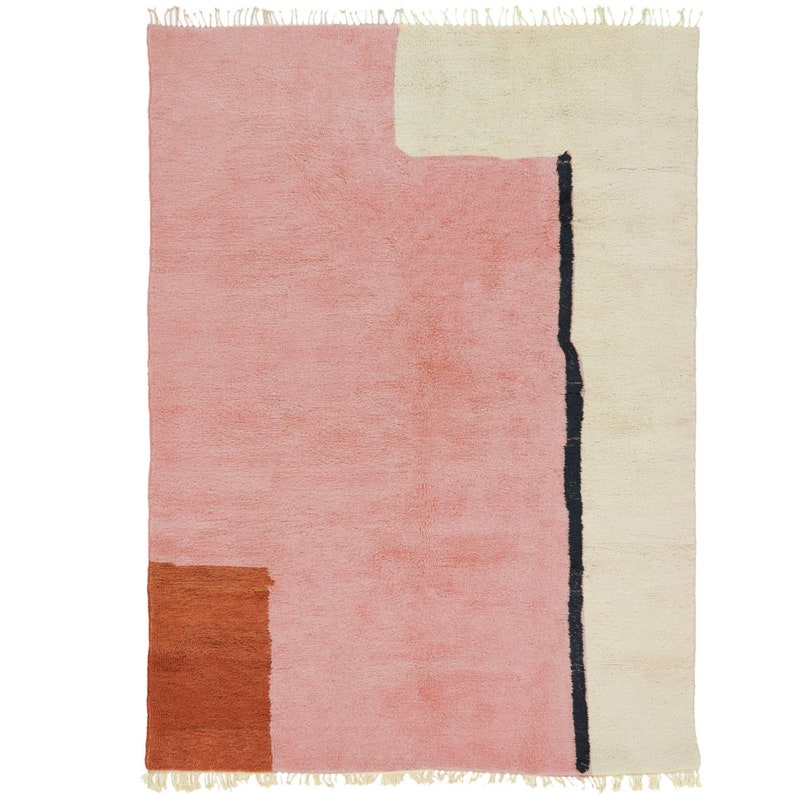 K&ouml;nnte beinhalten: Ein rosa und cremefarbener Teppich mit geometrischem Muster. Der Teppich hat eine schwarze Linie, die in der Mitte verl&auml;uft, und ein braunes Rechteck in der linken unteren Ecke.