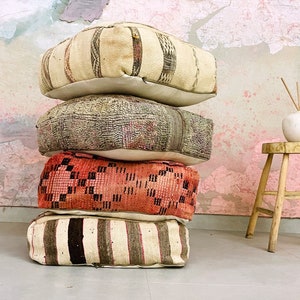 May include: A stack of four colorful, patterned floor cushions, made of woven fabric, with a white base. The cushions are stacked on top of each other, with the largest cushion on the bottom and the smallest cushion on top. The cushions are in a variety of colors, including red, brown, white, and gray.