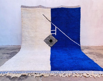 May include: A white and blue Moroccan rug with a geometric design. The rug has a fringe border and is made of wool.
