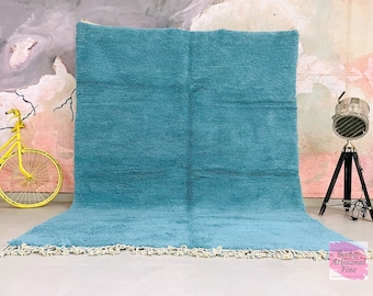 May include: A light blue Moroccan rug with a fringe border. The rug is made of wool and has a soft, textured feel.