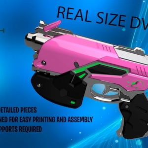 May include: A 3D printed model of a pink and green D.Va gun from the video game Overwatch. The model is labelled "REAL SIZE DVA GUN" and "DIY!" and includes the text "#HIGH DETAILED PIECES #DESIGNED FOR EASY PRINTING AND ASSEMBLY # NO SUPPORTS REQUIRED".