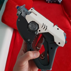 May include: A white and black toy gun with a black handle and a white barrel. The gun has a silver detail on the top and a black trigger.
