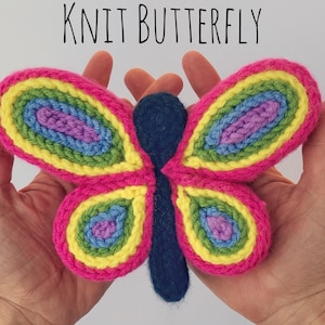 May include: A handmade, knitted butterfly in vibrant colors. The wings are pink with yellow, green, blue, and purple details. The body is dark blue. The text "KNIT BUTTERFLY" is above the butterfly.