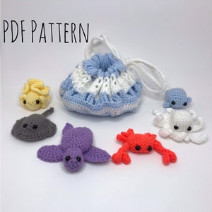 May include: A crocheted drawstring bag with a blue and white striped pattern. The bag is filled with crocheted sea creatures, including a yellow seahorse, a gray stingray, a purple turtle, a red crab, and a white octopus with a blue head.