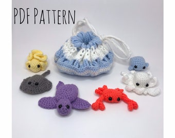 May include: A crocheted drawstring bag with a blue and white striped pattern. The bag is filled with crocheted sea creatures, including a yellow seahorse, a gray stingray, a purple turtle, a red crab, and a white octopus with a blue head.