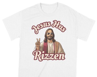 May include: White t-shirt with a cartoon image of Jesus wearing sunglasses and giving a peace sign. The text "Jesus Has Rizzen" is printed in red on the shirt.