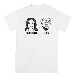May include: White t-shirt with black and white images of Kamala Harris and Donald Trump. The text "Prosecutor" is below Harris's image and "Felon" is below Trump's image.