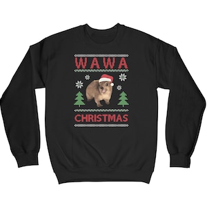 Puede incluir: Sudadera negra con un diseño navideño de color blanco, rojo y verde. El diseño presenta un quokka con un gorro de Papá Noel, dos árboles de Navidad, copos de nieve y el texto "Wawa Christmas".