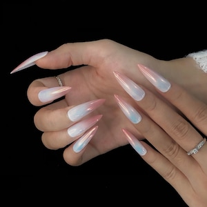 Op de afbeelding: Lange stiletto-vormige press-on nagels met een parelmoer afwerking en een zacht kleurverloop van een lichtroze punt naar een melkwitte basis. De nagels hebben een glad, reflecterend oppervlak met subtiele iriserende accenten.