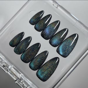 May include: A set of ten almond-shaped press-on nails featuring a dark, magnetic cat-eye finish. The surface displays a deep teal and black base with shimmering, holographic glitter particles that create a reflective, multi-dimensional effect.