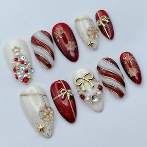 May include: A set of ten press-on nails featuring a Christmas theme with red and white glossy finishes. Designs include gold glitter snowflakes, raised gold bows, candy cane stripes, and embellishments of red and white pearls and crystals.