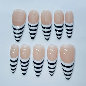 May include: A set of ten artificial nails with a nude base and black and white striped design. The nails are in various sizes and shapes, with a glossy finish, perfect for a manicure.