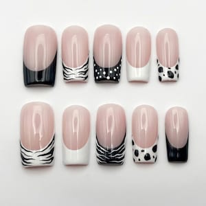 May include: A set of ten press-on nails with a nude base and various black and white tip designs, including solid black, zebra stripes, white polka dots, solid white, and cow print patterns, arranged in two rows against a plain white background.