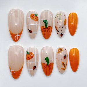 May include: A set of ten almond-shaped press-on nails featuring a nude base with orange French tips, white grid patterns, hand-painted orange pumpkins, brown acorns, and autumn leaves. The design includes small white star accents and dots.