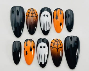 Pode incluir: Um conjunto de dez unhas postiças em formato amendoado com tema de Halloween. Os designs incluem unhas pretas brilhantes, unhas laranja com teias de aranha pretas, figuras de fantasmas brancos em fundo preto e unhas laranja com gotas pretas.